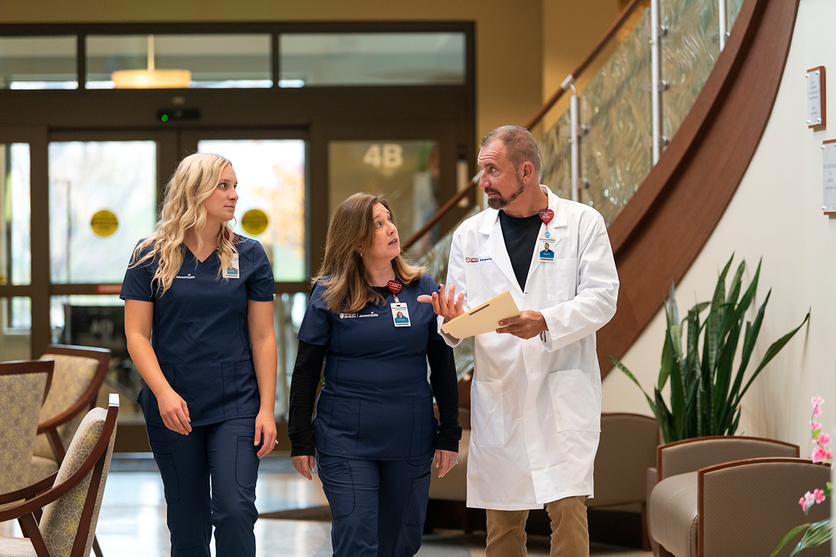 AdventHealth Three clinicians walking across a hospital lobby.