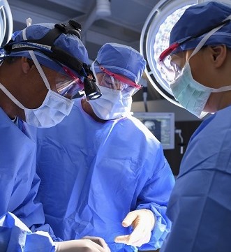 Nurse Practitioner Pic Three surgeons in blue surgical gowns and masks performing a procedure in an operating room.